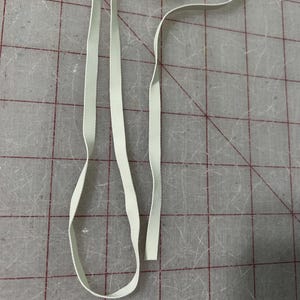 Puede incluir: Tres tiras elásticas blancas, probablemente para proyectos de costura o manualidades.