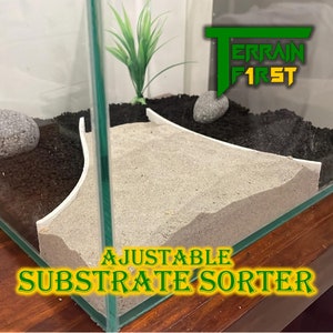 Puede incluir: Un separador de sustrato ajustable de plástico blanco para un terrario. El separador tiene forma de rampa curva y se coloca en un tanque de vidrio con sustrato negro y blanco. El texto "ADJUSTABLE SUBSTRATE SORTER" es visible en la imagen.