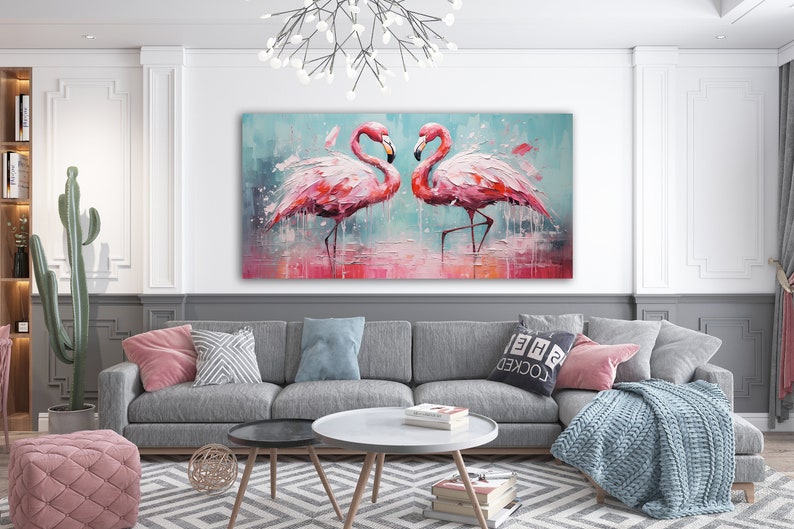 May include: A painting of two pink flamingos standing in a shallow body of water. The flamingos are facing each other and their heads are touching. The painting is in a modern living room setting, hanging above a gray couch with pillows.