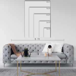 May include: A white wall with a gray couch and a coffee table in front of it. The wall has five different sized white frames with black text indicating the dimensions of each frame in inches. The text reads: 48x32, 36x24, 30x20, 24x16, 16x12. The text "5 ft" is written below the frames.