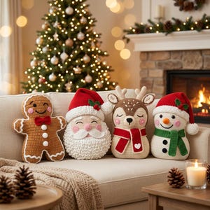 Puede incluir: Cuatro cojines de ganchillo con forma de personajes navideños: un hombre de jengibre marrón, un Santa Claus con gorro rojo, un reno beige con bufanda roja y un muñeco de nieve blanco con gorro rojo y bufanda verde, todos con detalles bordados.