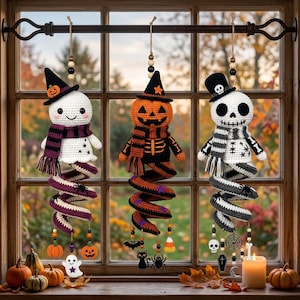 May include: Three hanging crochet Halloween decorations featuring a ghost with a purple scarf, a pumpkin figure with an orange scarf, and a skeleton with a grey scarf. Each figure has a spiral tail, wooden beads, and small dangling charms.
