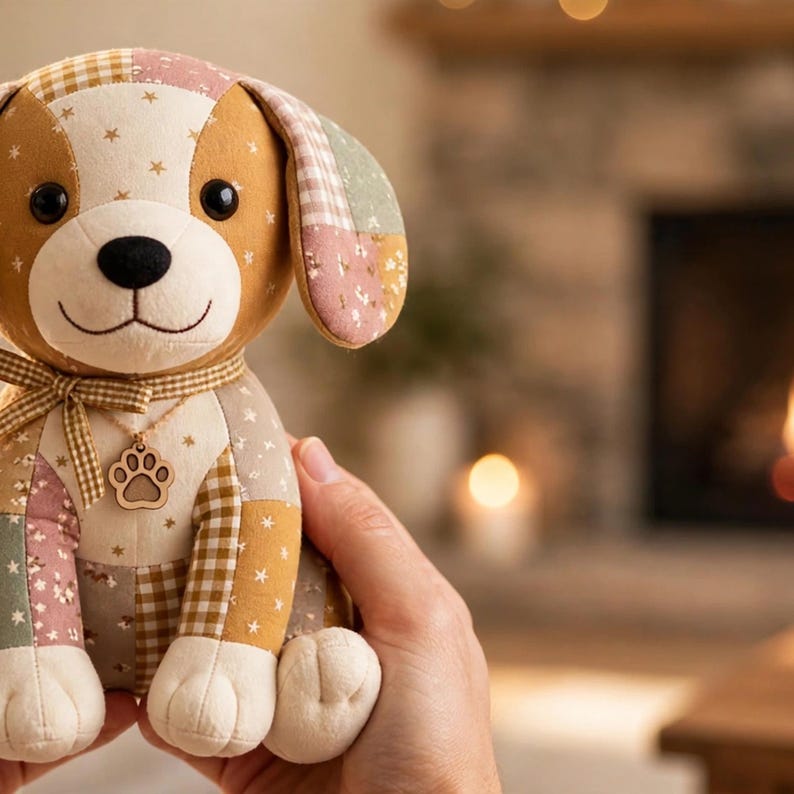 May include: A plush dog toy made of patchwork fabric in shades of tan, cream, and muted pink. The dog features a gingham ribbon around its neck with a wooden paw print charm, black button eyes, and a stitched nose, with star and floral patterns.