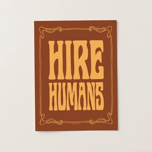 A gold on bronze art print of the words HIRE HUMANS in a hand-lettered art nouveau style within a decorative art nouveau border.