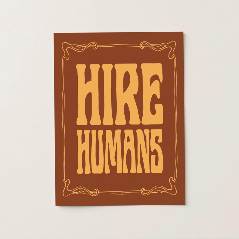 A gold on bronze art print of the words HIRE HUMANS in a hand-lettered art nouveau style within a decorative art nouveau border.