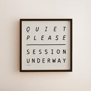 Könnte beinhalten: Gerahmter Druck mit den Worten "QUIET PLEASE SESSION UNDERWAY" in schwarzen, handschriftlichen Buchstaben auf weißem Hintergrund. Der Druck befindet sich in einem dunkelbraunen Rahmen und ist an einer hellbeigen Wand befestigt.