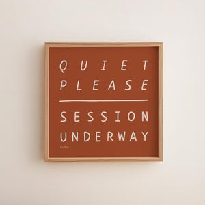 Könnte beinhalten: Gerahmter Wandkunstdruck mit den weißen Worten "QUIET PLEASE SESSION UNDERWAY" auf terrakottafarbenem Hintergrund. Das Kunstwerk hat einen Holzrahmen und ein minimalistisches Design.