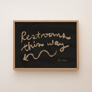 Restrooms This Way - Hand-lettered navigational sign, left. Cream on black.