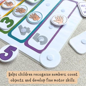 May include: An educational counting activity sheet featuring colorful numbers and circular tokens with hand illustrations showing fingers. The board includes velcro dots for attaching tokens, with text stating: Helps children recognize numbers, count objects, and develop fine motor skills.