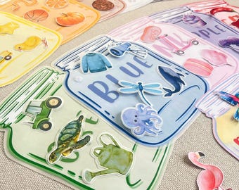 May include: A collection of colorful jar-shaped stickers, each with a different theme. One jar is labeled "BLUE" and features a sweater, dragonfly, and whale. Other jars showcase various objects, including a tractor, turtle, and flamingo.