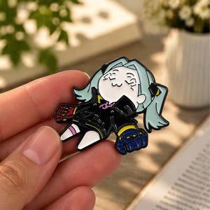 Könnte beinhalten: Ein farbenfroher Emaille-Pin mit einer Zeichentrickfigur mit hellblauen Haaren und einem schwarzen Outfit. Der Pin hat rote und blaue Akzente auf den Handschuhen und befindet sich in einer entspannten Pose. Der Pin ist ein Sammlerstück.
