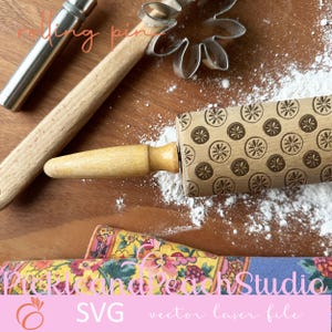 May include: A wooden rolling pin with a brown and white design of lemons. The rolling pin is on a wooden surface with white powder and a metal cookie cutter in the background.