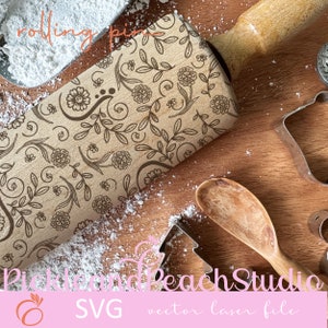 May include: A wooden rolling pin with a floral design engraved on the surface. The rolling pin is surrounded by white powder and other baking tools.