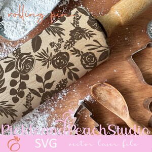 May include: A wooden rolling pin with a brown floral design. The rolling pin is on a wooden surface with a spoon and cookie cutters.