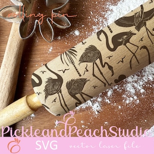 May include: A wooden rolling pin with a brown and black design of flamingos, palm trees, and birds. The rolling pin is on a wooden surface with white powder.