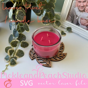 Könnte beinhalten: Ein hölzerner, blattartiger Kerzensockel mit einer rosa Kerze darauf. Die Kerze hat drei Dochte. Der Text "leaves trivet candle base" steht über der Kerze. Der Text "PickleandPeachStudio SVG vector laser file" steht unter der Kerze.