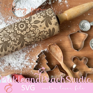 Peut inclure: Un rouleau à pâtisserie en bois avec un motif floral, entouré d'emporte-pièces et de sucre glace sur une surface en bois. Le rouleau à pâtisserie est étiqueté "rolling pin".