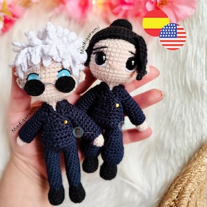 May include: Two handmade crochet dolls, one with white hair and round black glasses, the other with black hair. Both dolls wear navy blue suits with gold buttons. The dolls are held in a hand, with the text "Madigurumi" visible.