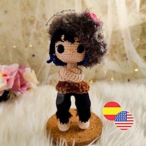 May include: Crocheted amigurumi doll of a character with black hair, blue accents, and a furry gray head covering with a pink flower. The doll wears black pants and a brown belt. The doll is standing on a cork base.
