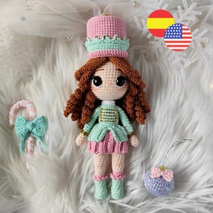 Puede incluir: Muñeca de ganchillo hecha a mano con forma de cascanueces. La muñeca tiene pelo rizado castaño, un sombrero rosa y verde, y un atuendo a juego. También se ven un bastón de caramelo y un pequeño adorno.