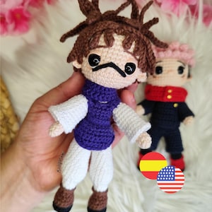 Puede incluir: Muñecos de ganchillo hechos a mano que representan personajes de anime. Uno tiene cabello castaño y una parte superior morada, el otro tiene cabello rosado y un uniforme negro. Los muñecos están intrincadamente elaborados con rasgos faciales y ropa detallados. Flores rosas en el fondo.