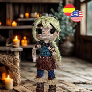 Puede incluir: Una muñeca de ganchillo con cabello rubio, grandes ojos negros y pestañas largas. La muñeca viste un top verde azulado, una falda marrón con detalles plateados, leggings azules y botas marrones con ribete de piel beige. El texto Madigurumi es visible.