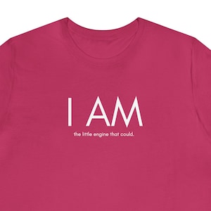 Könnte beinhalten: Ein pinkfarbenes T-Shirt mit dem Aufdruck "I AM the little engine that could." in weiß.