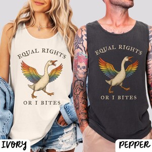 Puede incluir: Camisetas sin mangas de color marfil y pimienta con un gr&aacute;fico de ganso arco&iacute;ris y el texto "EQUAL RIGHTS OR I BITES". El ganso tiene alas de arco&iacute;ris y est&aacute; caminando. Las camisetas sin mangas son sin mangas.