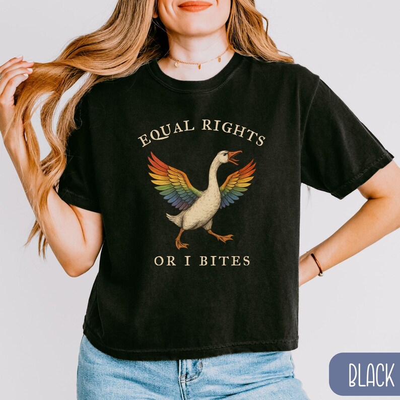 Peut inclure: T-shirt noir avec l'inscription "EQUAL RIGHTS OR I BITES" et un dessin d'oie aux ailes arc-en-ciel. L'oie est repr&eacute;sent&eacute;e avec le bec ouvert et une patte lev&eacute;e, pour un design amusant et accrocheur.