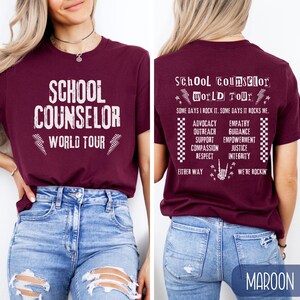 K&ouml;nnte beinhalten: Ein maroonfarbenes T-Shirt mit dem Text "School Counselor World Tour" auf der Vorderseite und einer Liste von W&ouml;rtern im Zusammenhang mit Schulberatung auf der R&uuml;ckseite. Die W&ouml;rter auf der R&uuml;ckseite umfassen "Advocacy", "Empathy", "Outreach", "Guidance", "Support", "Empowerment", "Compassion", "Justice", "Respect" und "Integrity".