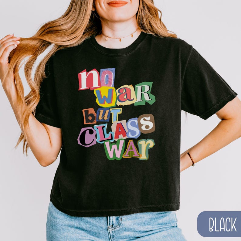 May include: Black t-shirt with the text "no war but class war" in a colorful, cut-out style. The shirt is a crew neck and has short sleeves. The model is wearing blue jeans.