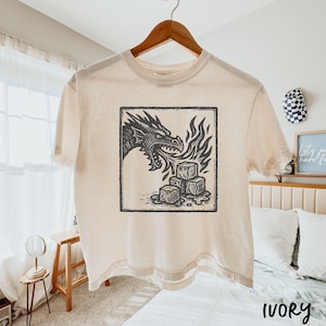 May include: Ivory t-shirt with a black and white dragon graphic breathing fire onto ice cubes, framed in a square. The shirt is displayed on a wooden hanger. The word "IVORY" is printed at the bottom.