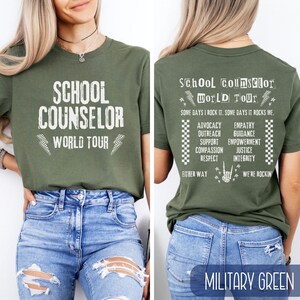 K&ouml;nnte beinhalten: Ein gr&uuml;nes T-Shirt mit dem Text "School Counselor World Tour" auf der Vorderseite und einer Liste von W&ouml;rtern, die mit dem Beruf zu tun haben, auf der R&uuml;ckseite. Der Text ist wei&szlig; und das Shirt ist milit&auml;rgr&uuml;n.