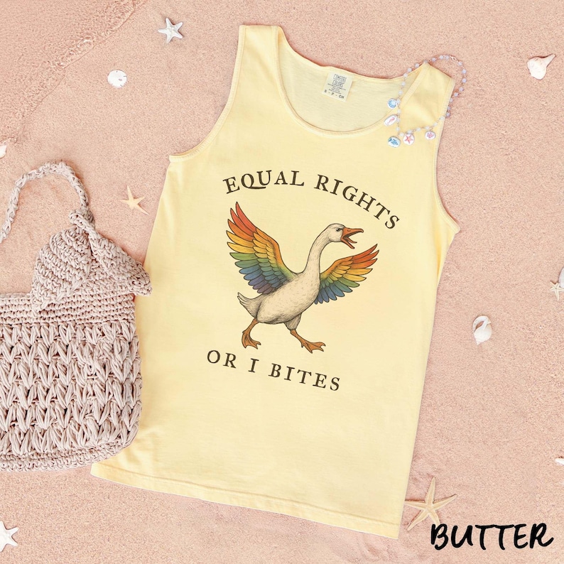 Puede incluir: Una camiseta sin mangas de color amarillo claro con el texto "EQUAL RIGHTS OR I BITES" y un ganso con alas de arco&iacute;ris. A la izquierda hay un bolso de ganchillo beige. La palabra "BUTTER" est&aacute; en la parte inferior derecha.