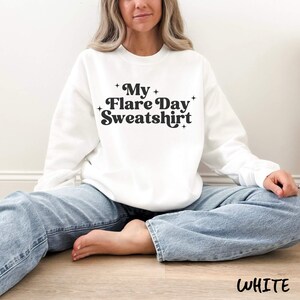 May include: A white sweatshirt with the text "My Flare Day Sweatshirt" in a black, retro font. The sweatshirt is a crew neck style and is made of a soft material. The word "WHITE" is at the bottom of the image.