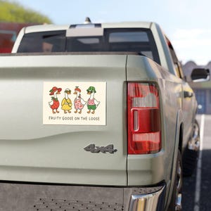 May include: A rectangular sticker featuring four cartoon geese dressed as fruits. The geese are wearing hats and outfits resembling a strawberry, a lemon, a cherry, and a watermelon. The text "FRUITY GOOSE ON THE LOOSE" is below the geese.