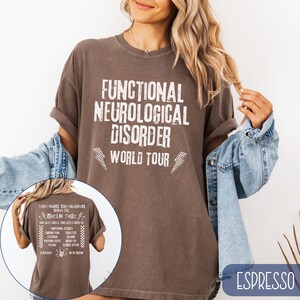K&ouml;nnte beinhalten: Ein braunes T-Shirt mit dem Aufdruck "Functional Neurological Disorder World Tour" auf der Vorderseite. Der Text ist in einer wei&szlig;en, abgenutzten Schriftart mit einem schwarz-wei&szlig;en Schachbrettmuster auf beiden Seiten.