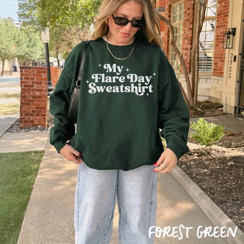 May include: A forest green sweatshirt with the text "My Flare Day Sweatshirt" in white. The sweatshirt is paired with light wash jeans. The words "Forest Green" are at the bottom of the image.