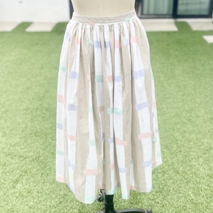 May include: A high-waisted midi skirt featuring a vertical striped pattern in beige and white. The fabric is decorated with small, horizontal brushstroke-style accents in soft pastel shades of light blue, mint green, and pale pink throughout.