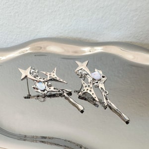 May include: A pair of silver earrings featuring a star design and iridescent stones. The earrings are drop earrings with a delicate, intricate design.