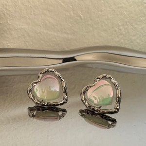 May include: A pair of silver heart-shaped earrings with iridescent pink and green stones.