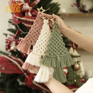 May include: Three handmade macrame Christmas tree ornaments in pink, white, and green with wooden star toppers.