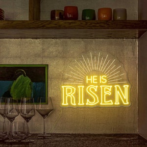 May include: A yellow neon sign with a sunburst design and the words "He is Risen" in a bold font.