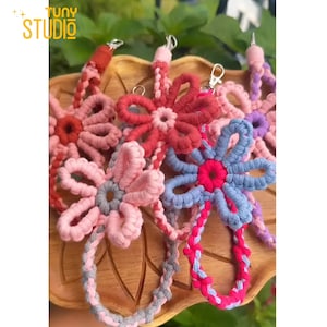Puede incluir: Primer plano de varios llaveros de flores de macramé hechos a mano en varios colores, incluyendo rosa, rojo y azul. Cada llavero presenta un diseño de flor con un nudo central y un lazo para sujetar las llaves. Los llaveros se muestran en una bandeja de madera.