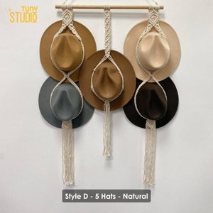 May include: Five hats hanging on a macrame hat rack with a wooden dowel. The hats are brown, beige, gray, and black. The macrame is natural colored. The text "Style D - 5 Hats - Natural" is at the bottom of the image.