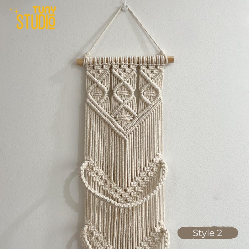 May include: Cream-colored macrame wall hanging with geometric and curved patterns. The wall decor is suspended from a wooden dowel and features the text "TINY STUDIO" in yellow. Style 2 is indicated in a brown rectangle.