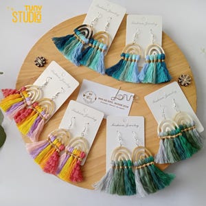 May include: Five pairs of rainbow-colored tassel earrings with wooden rainbow-shaped charms. The earrings are displayed on white cards with the text "Fashion Jewelry" printed on them.