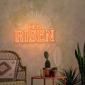 May include: A neon sign with a white outline and orange glow reads "He is Risen" with a sunburst design behind the text.