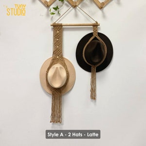 May include: Two hats hanging on a macrame wall decor with a wooden dowel. The hats are brown and beige. The macrame is made of natural jute rope and has a fringe. The text "Style A - 2 Hats - Latte" is at the bottom of the image.