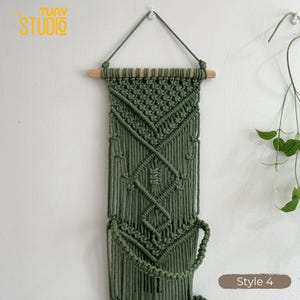 May include: A handcrafted macrame wall hanging in olive green. The wall decor features intricate knotting patterns, a wooden dowel, and a hanging loop. The text "Tuny Studio" is in the upper left corner, and "Style 4" is in the lower right corner.